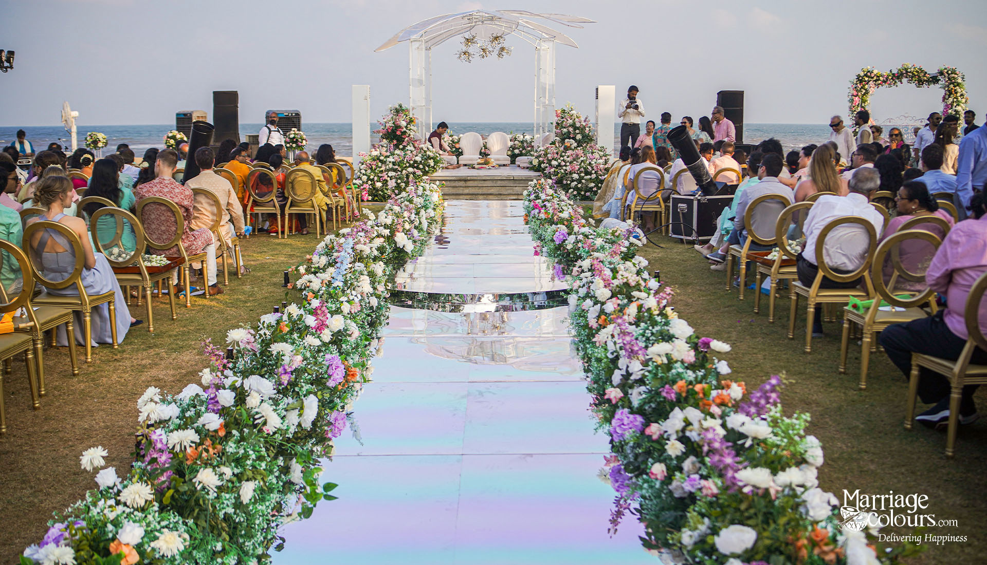 Guests seated along a reflective aisle with fresh floral arrangements at an Intercontinental Destination Wedding in Mahabalipuram, with a luxury floral and fabric mandap for an Indian beach wedding ceremony.