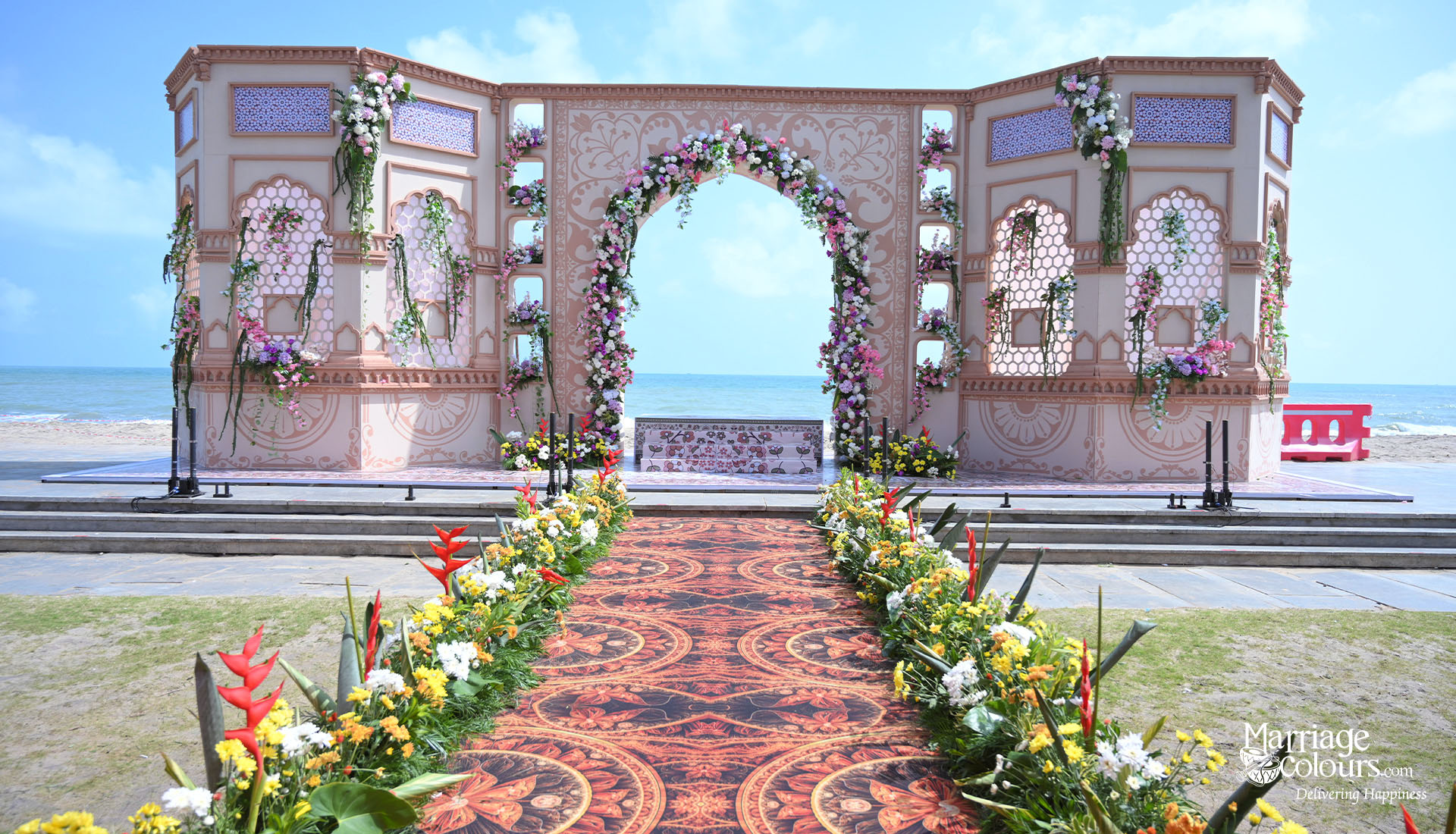 An Indian couple under an ornate floral and fabric mandap and a traditional palatial backdrop for a Varmala ceremony at a luxury destination wedding in Mahabalipuram.