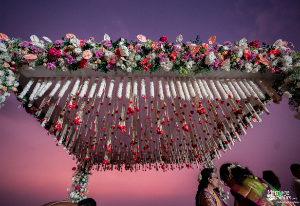 Close-up of a floral mandap ceiling with white tube-shaped hangings and small red flower tassels.