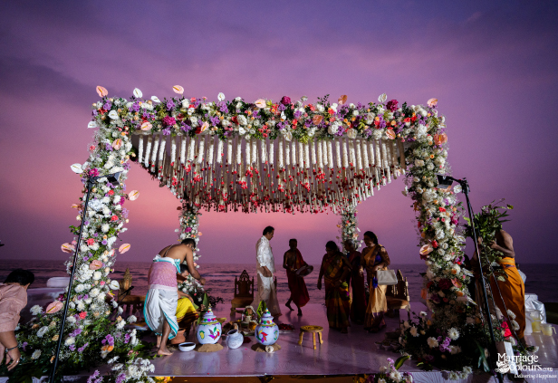 Hindu wedding ceremony under a floral mandap on the beach with a breathtaking purple sunset sky.