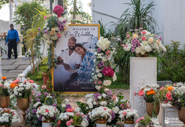"Welcome to Our Wedding" sign for Aishwarya & Shanthan, surrounded by abundant, colorful fresh flowers.