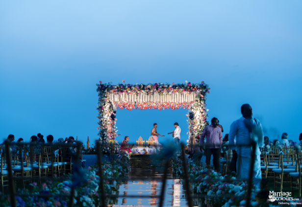 Beach wedding ceremony under a floral mandap and clear twilight sky with a mirrored aisle