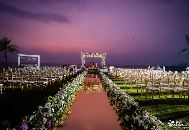 Spectacular beach wedding setup with mirrored aisle, gold chairs, and floral mandap at pink sunset.
