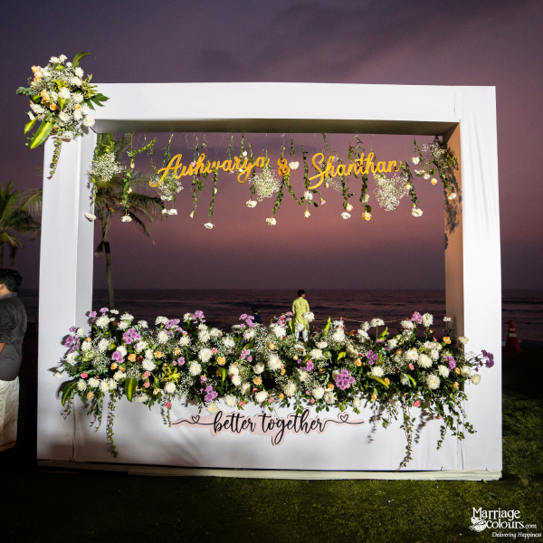 Large white frame decorated with flowers and "Aishwarya & Shanthan" set against a twilight ocean sky