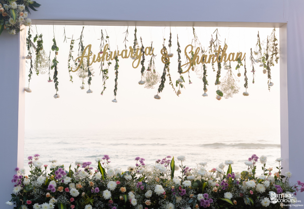 Wedding frame decoration with names Aishwarya & Shanthan, hanging flowers, and an ocean backdrop.
