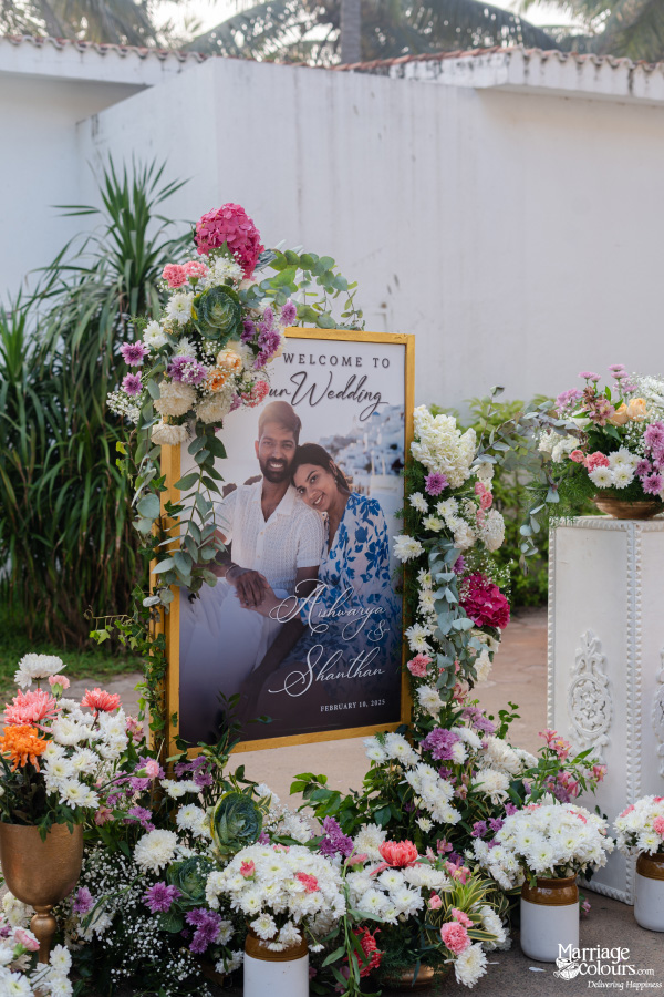 Wedding welcome sign featuring a photograph of Aishwarya and Shanthan, surrounded by colorful flowers.