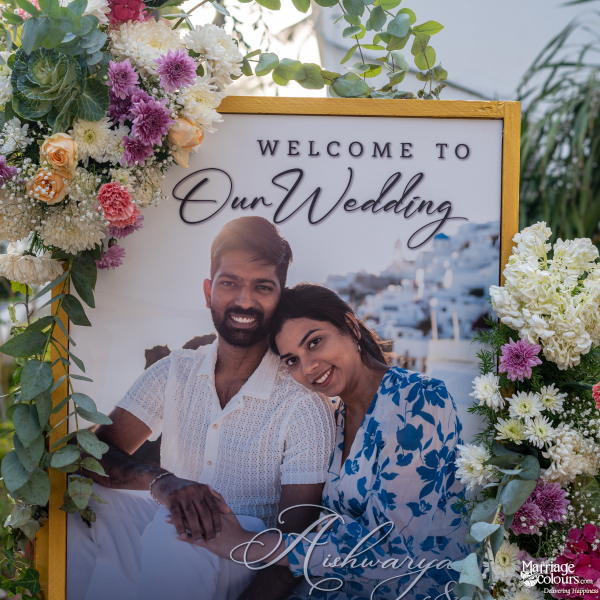 Wedding welcome sign with a photo of the smiling couple, Aishwarya and Shanthan, framed by flowers.