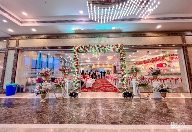 Wedding hall entrance with red and white floral arch, leading to an aisle with a red carpet.