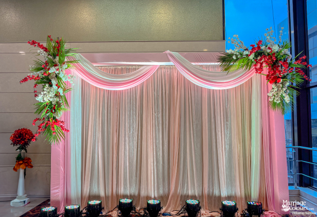 Elegant indoor wedding or reception stage decorated with pink draping and fresh red and white flowers.