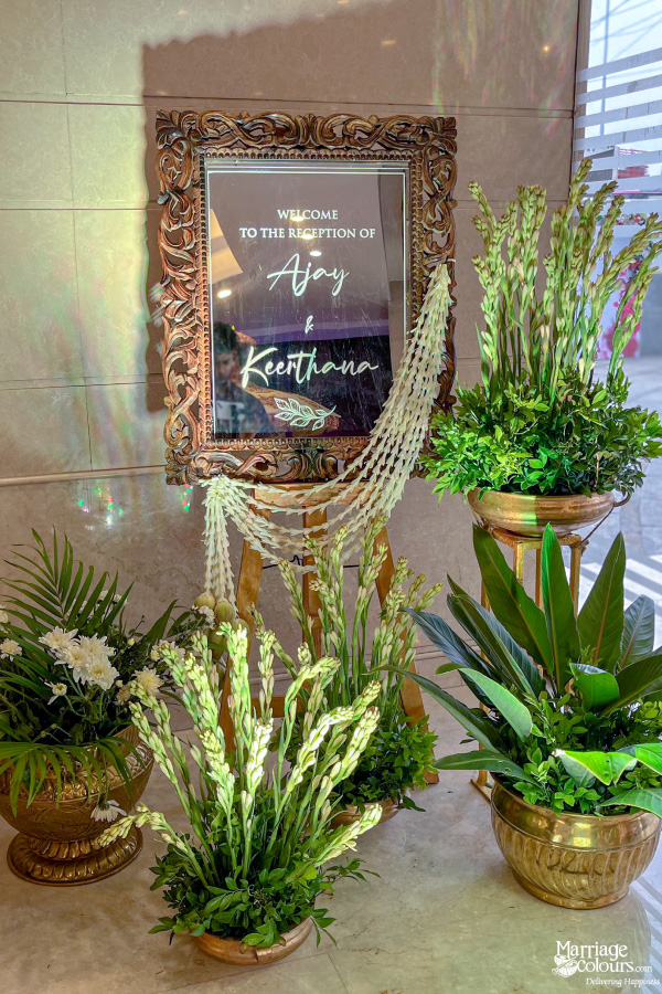 Ornate mirror signage reading "Welcome to the Reception of Ajay & Keerthana" surrounded by greenery.