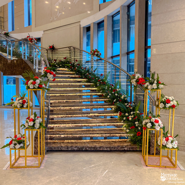 Grand marble staircase entrance decorated with white and red floral arrangements and greenery for a wedding.