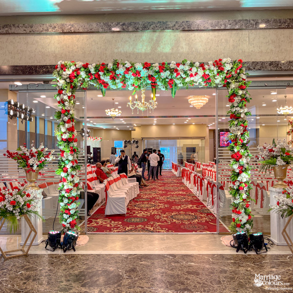 Wedding hall entrance with a red and white floral arch leading to an aisle with a red carpet.