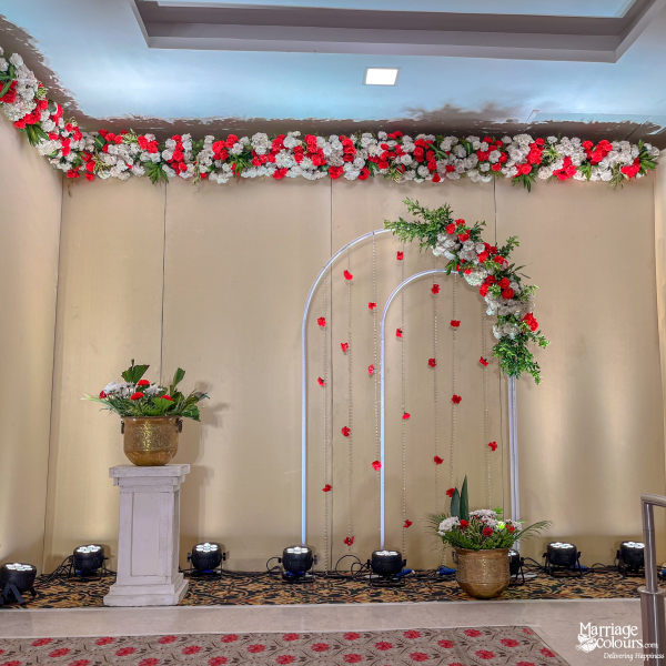 Wedding reception backdrop with white arched decor, hanging red petals, and red and white floral garlands.