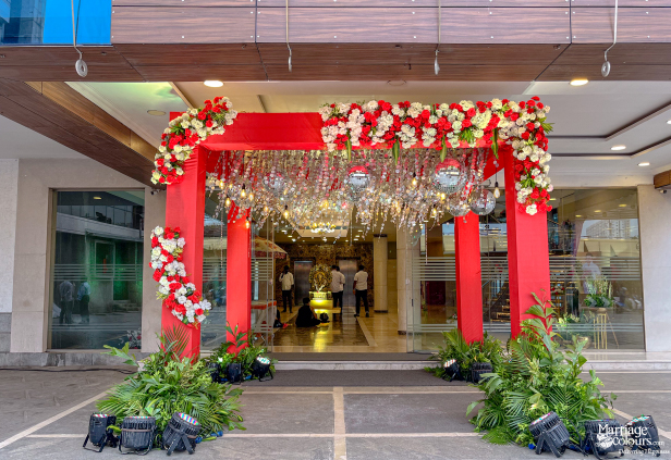 Red floral entrance arch with disco balls and a lush green border at a wedding venue.