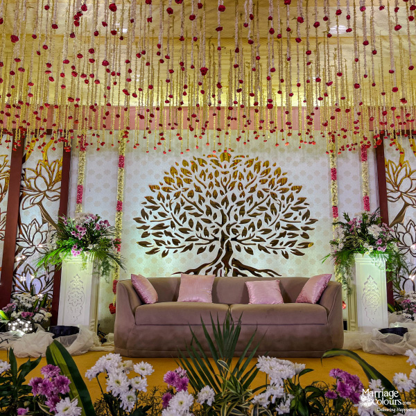 Romantic stage decor featuring a Tree of Life cutout, plush sofa, and hanging flower strings.
