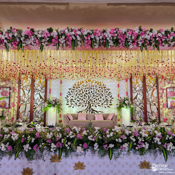 Wedding stage with Tree of Life backdrop, sofa, and a lush border of pink and white flowers.