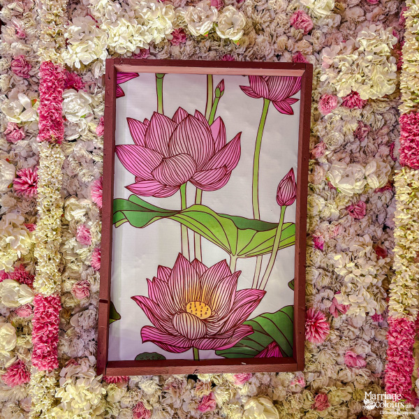 Close-up of a framed pink lotus illustration surrounded by a dense wall of pink and white flowers.