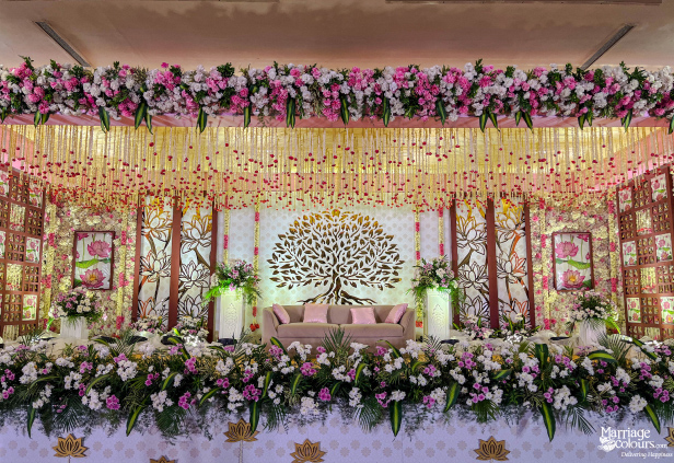 Romantic wedding reception stage with a Tree of Life motif, pink sofa, and extensive pink floral canopy.