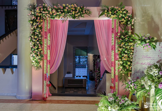 Wedding reception entrance arch framed with pink drapes, lush flowers, and long vertical garlands.