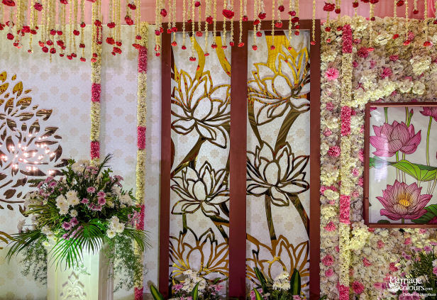 Wedding decor featuring gold lotus wall panels, a dense flower backdrop, and cascading floral strings.