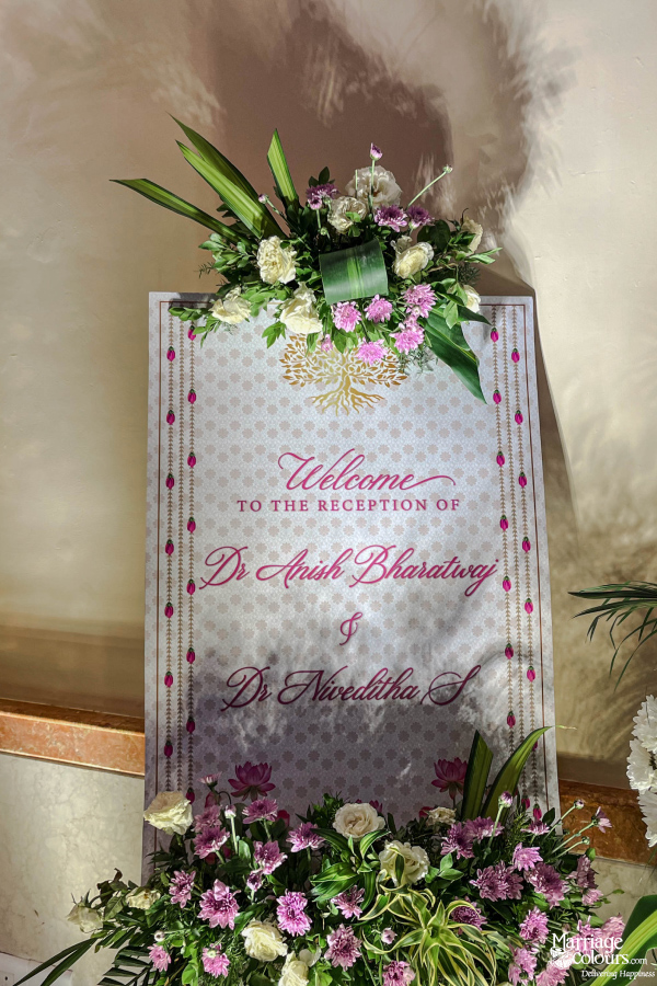 Welcome sign for Dr. Anish Bharadwaj and Dr. Niveditha S reception, decorated with white and purple flowers.