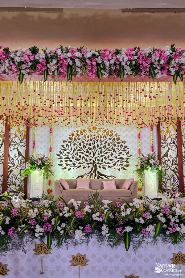 Reception stage with a beautiful golden Tree of Life backdrop and extensive pink and white flower decor.