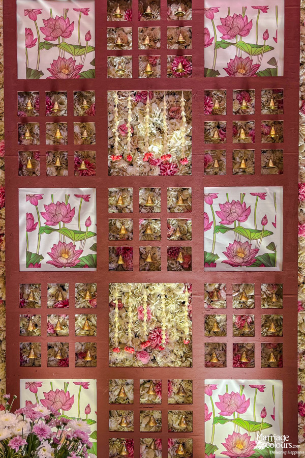 Intricate wedding backdrop with pink lotus prints, golden temple bells, and cascading pink and white flowers.