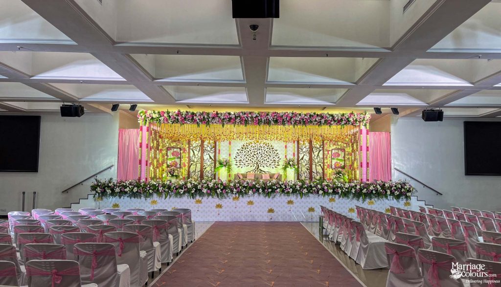Wedding reception stage with a Tree of Life backdrop, pink curtains, and extensive fresh floral decor.