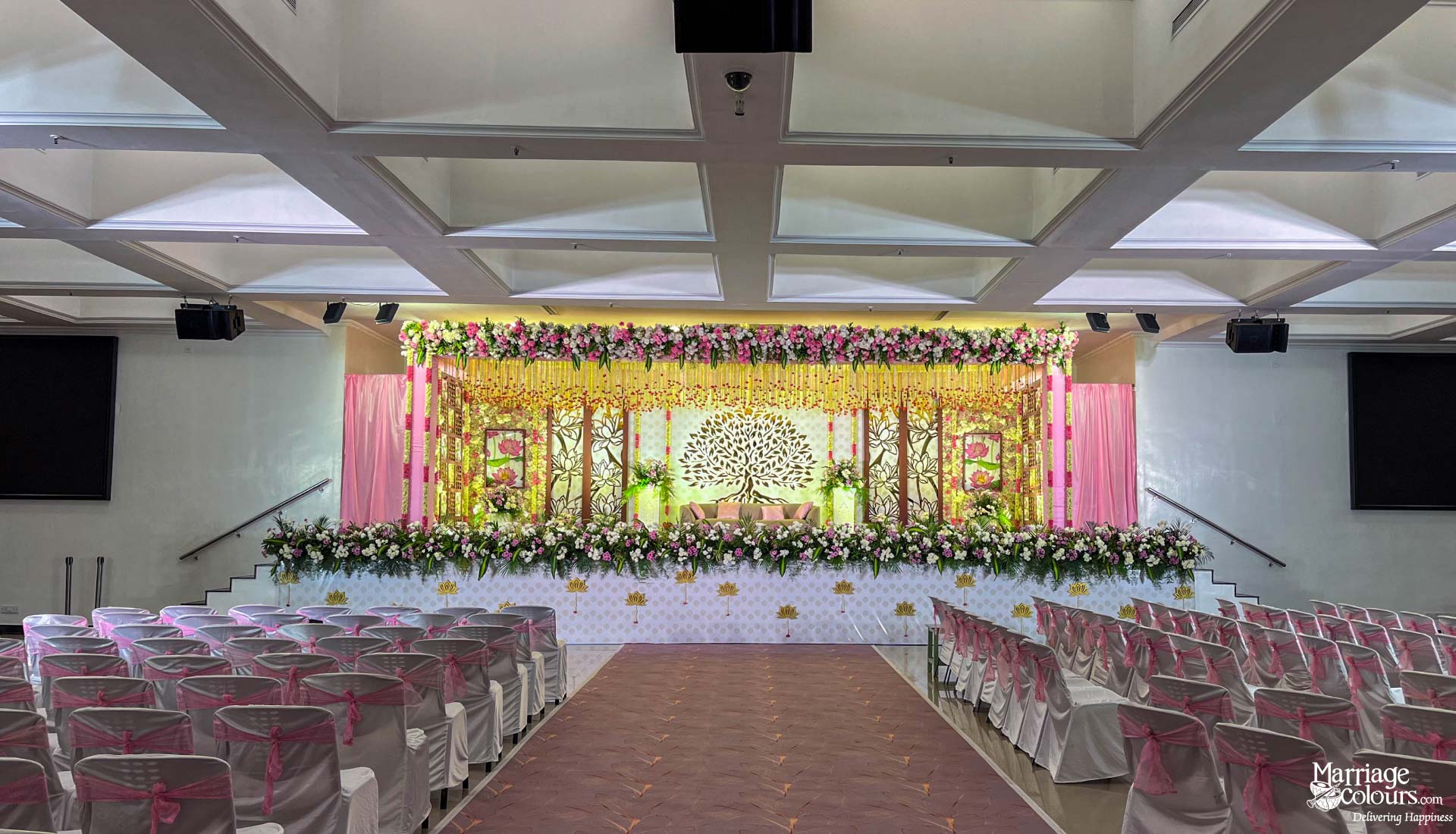 Wedding reception stage with a Tree of Life backdrop, pink curtains, and extensive fresh floral decor.