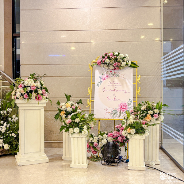 Welcome sign on gold easel, surrounded by white pedestals and pink and white flowers.