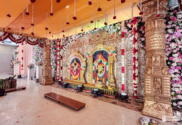 Traditional indoor stage with massive gold carved pillars and floral backdrop with idols.