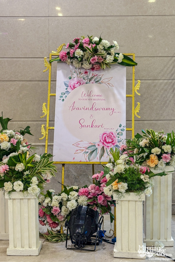 Welcome sign on gold easel, surrounded by white pedestals and pink and white flowers.