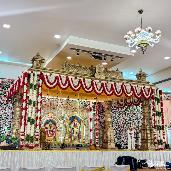 Grand traditional gold mandap on stage, covered with red, white, and pink flowers.
