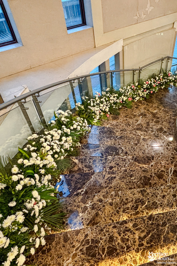 Marble staircase with glass railing decorated with a long garland of white flowers.