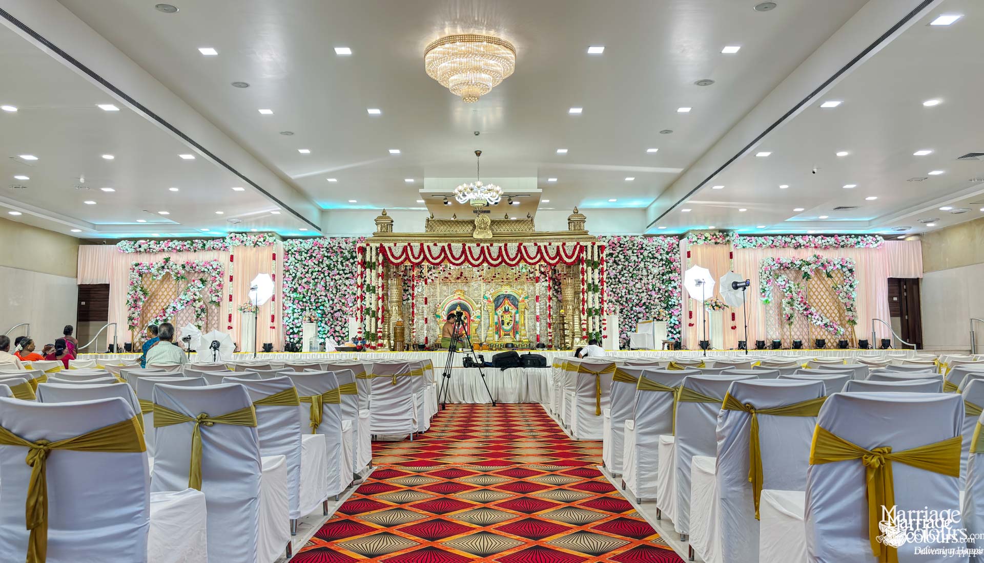 Wide view of a grand banquet hall with gold-draped chairs and a highly decorated stage.