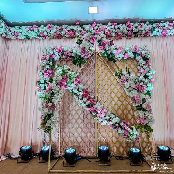 Photo booth backdrop with gold geometric frame, pink fabric, and white and pink flowers.