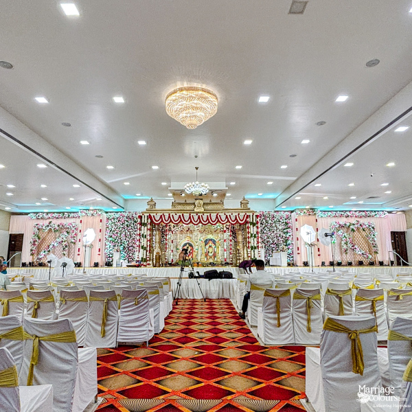 Wide view of a grand banquet hall with gold-draped chairs, red aisle, and stage.