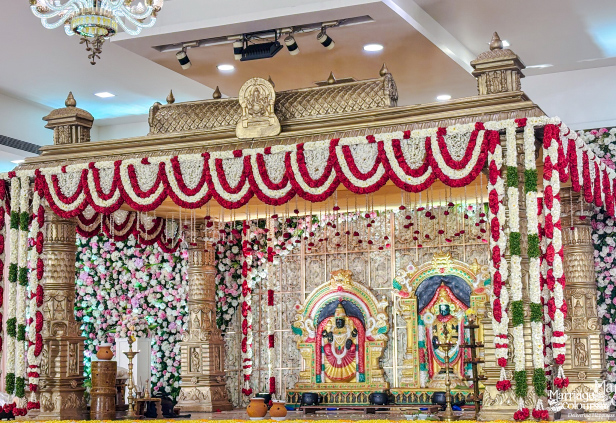 Grand traditional stage mandap with intricate gold pillars and red and white garlands.