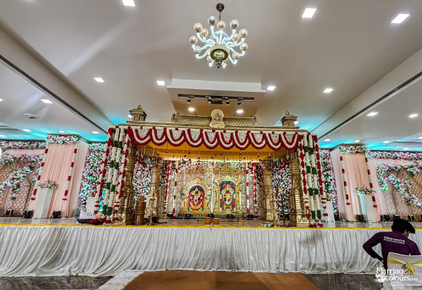 Wide view of traditional gold mandap on stage, decorated with white and red garlands.