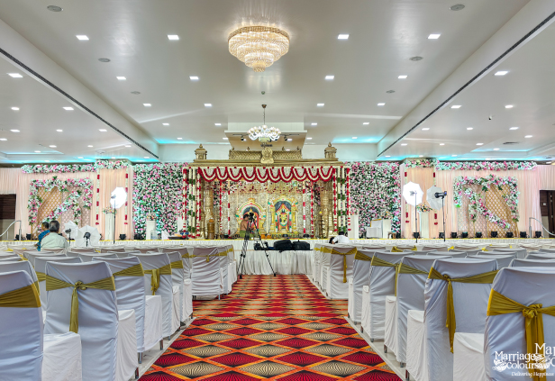 Wide view of a grand banquet hall with gold-draped chairs, red aisle, and stage.