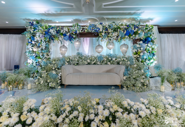 Stunning wedding stage with blue and white flowers, elegant sofa, and foreground of fresh blooms.