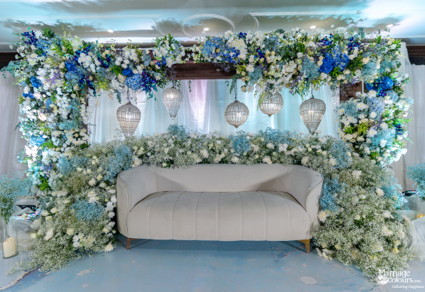 Symmetrical wedding stage featuring a white velvet sofa nestled among blue and white floral decor.