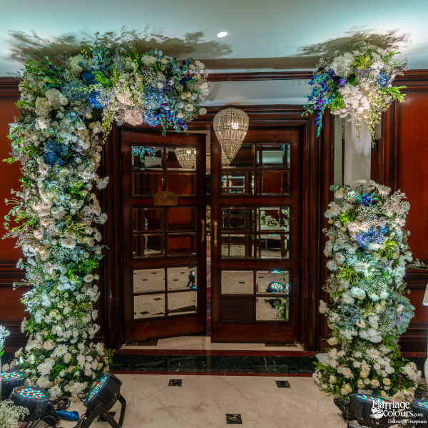 Wedding reception entrance featuring an elaborate arch of blue and white flowers around a wooden door.