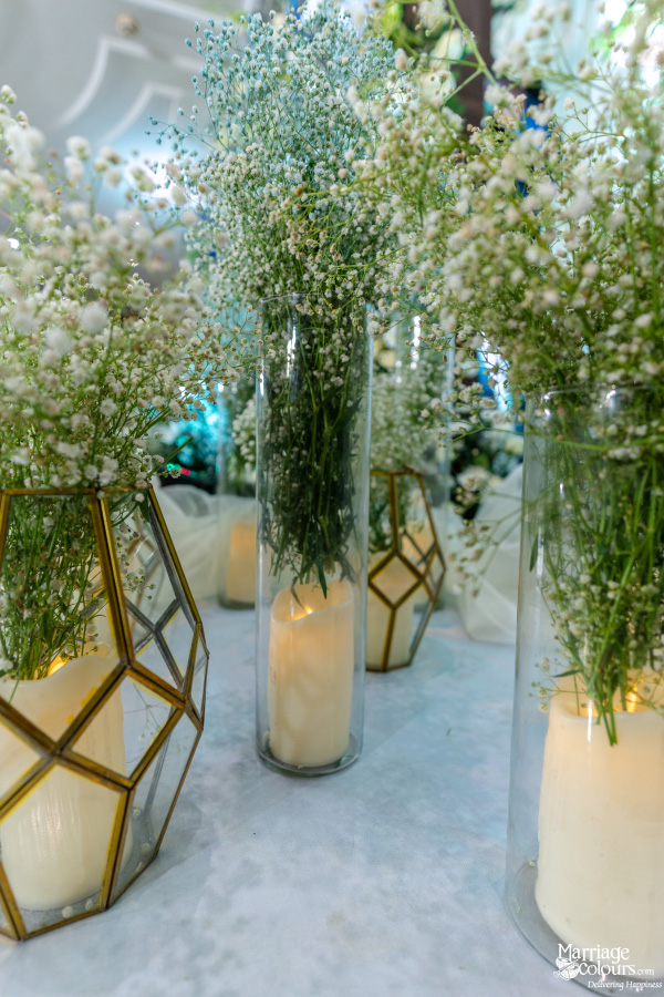 Wedding floor decor featuring tall vases of baby's breath flowers and glowing pillar candles.