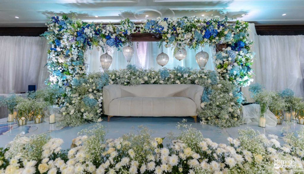 Opulent wedding stage decorated with lush blue and white flowers, baby's breath, and silver chandeliers.