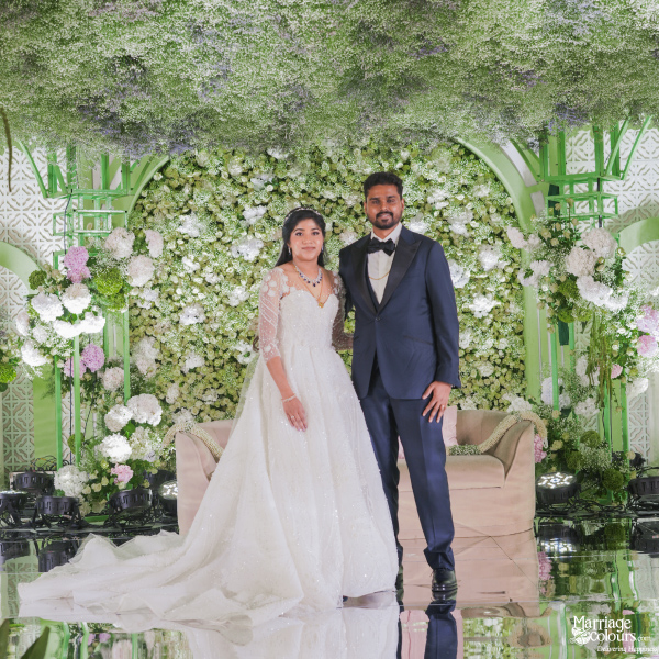 A newlywed couple posing formally in front of a stunning wedding stage with lush floral decor.