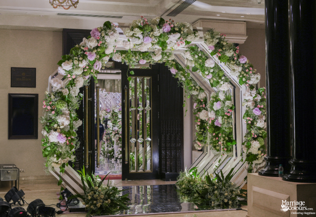 Grand wedding entrance featuring a modern geometric arch decorated extensively with white and pink flowers.
