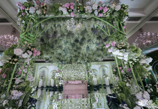 A grand, beautifully decorated wedding stage with a greenery canopy and pastel floral borders.