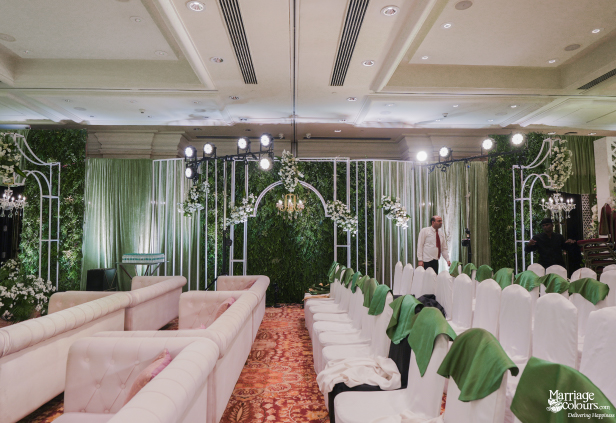 Setup of a wedding ceremony hall with white guest seating and a lush green backdrop stage.