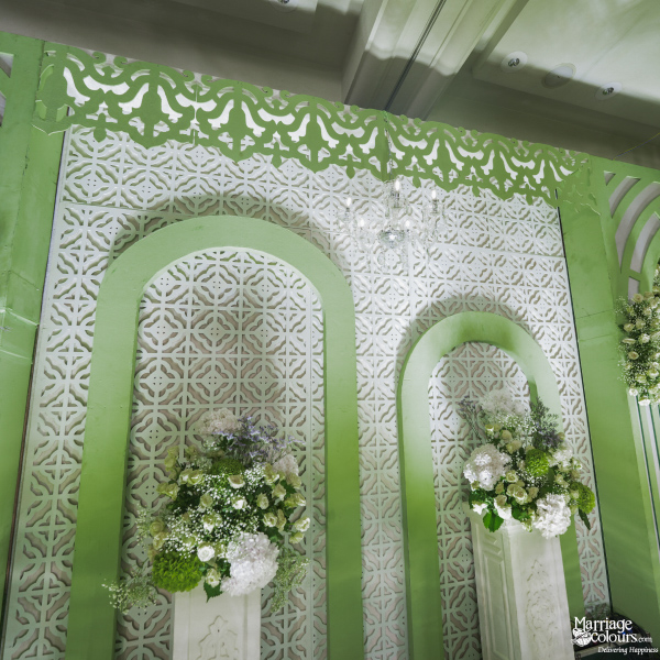 Close-up of stage backdrop featuring pale green arches, white lattice work, and floral arrangements.